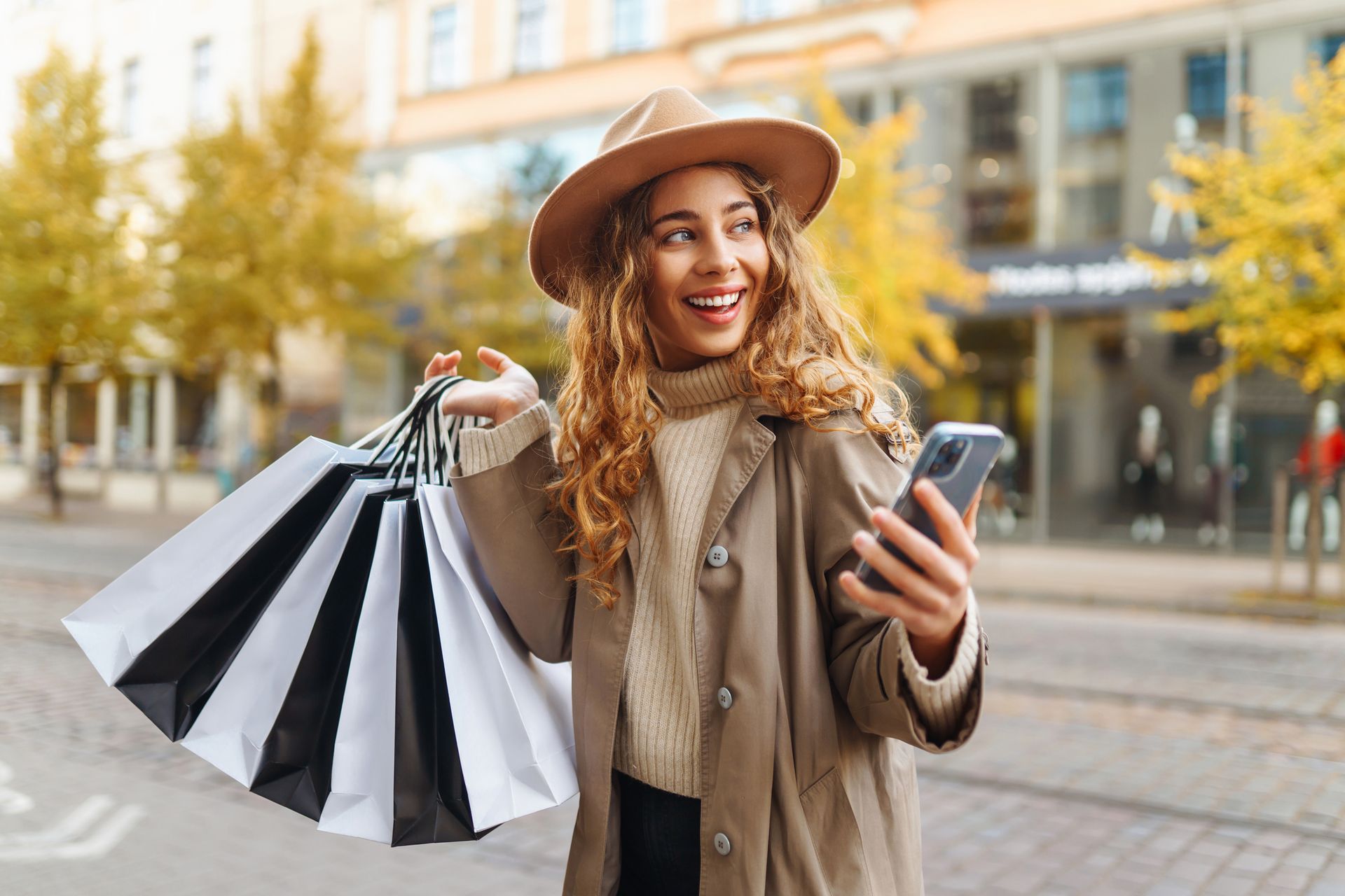 Shoppende Frau mit Hut schaut auf Mobiltelefon
